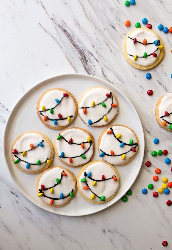 round cookies with white icing, m&ms used for lights, placed in white plate, christmas cookie icing, placed on marble countertop