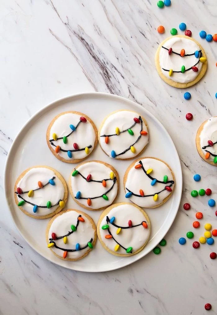 round cookies with white icing, m&ms used for lights, placed in white plate, christmas cookie icing, placed on marble countertop