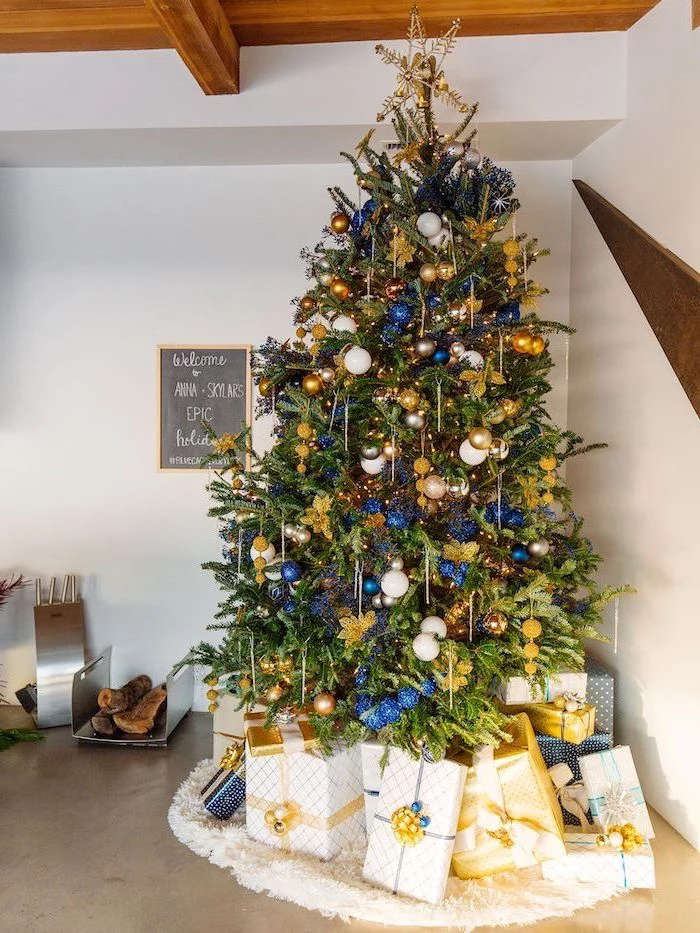 blue white and gold ornaments, tall tree with a star topper, elegant christmas tree decorating ideas, placed on white rug, wrapped presents underneath
