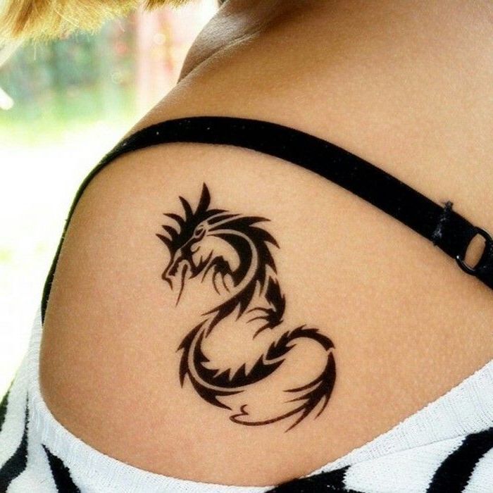 shoulder tattoo, dragon tattoos for women, woman with blonde hair, black and white sweater, black strap
