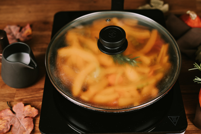 black skillet covered with a lid, potato soup recipe, jug of milk on the side, wooden table with fall leaves on it