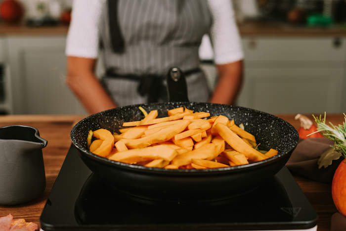 potato soup recipe, sliced pumpkin, cooking in a black skillet, placed on hot plate on wooden table