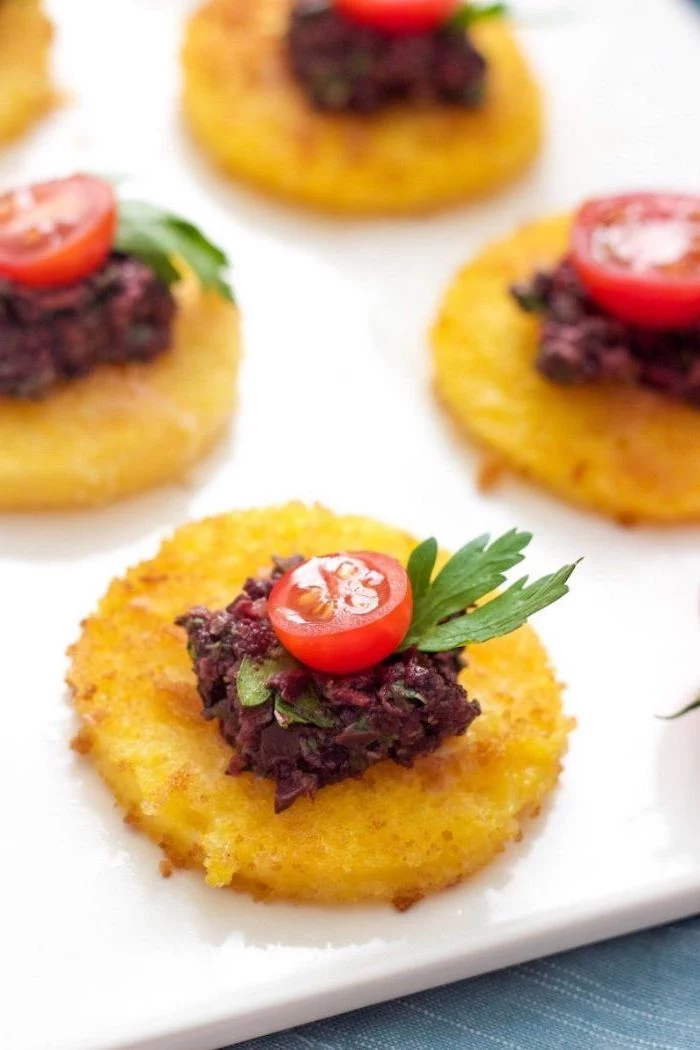 small hash brow bites with beet dip, halved cherry tomatoes on top, arranged on white plate, make ahead christmas appetizers