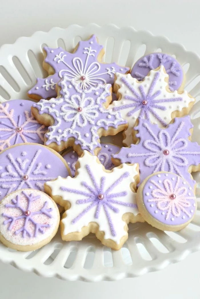 snowflake shaped cookies, decorated with purple and white icing, royal icing christmas cookies, placed in white bowl