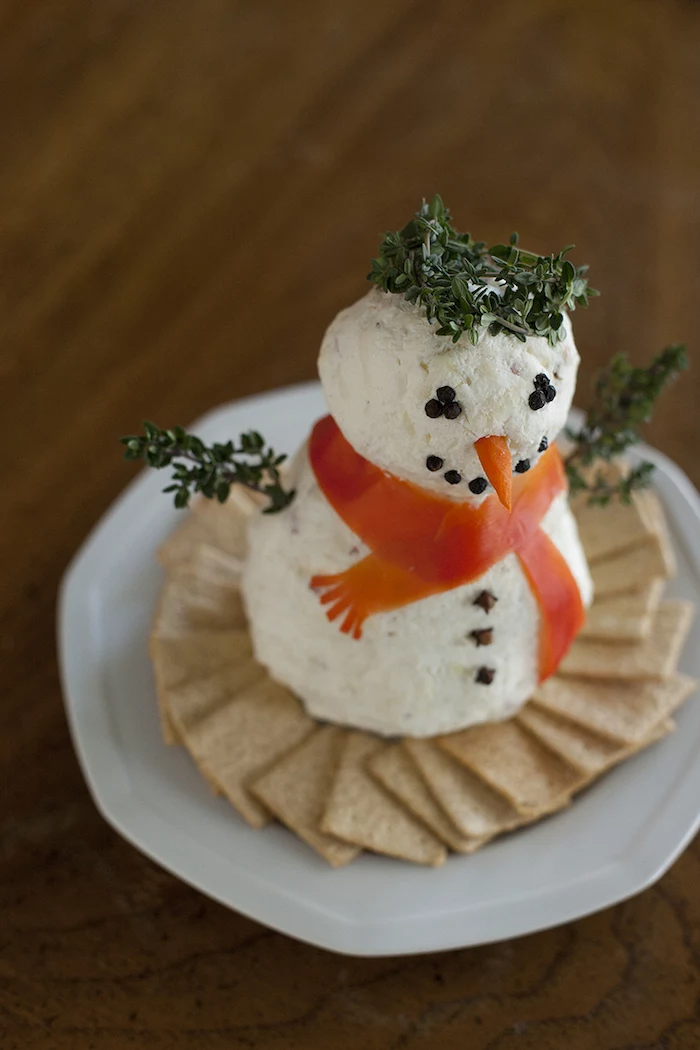 christmas eve appetizers, snowman made of cheeseballs and herbs, crackers on the side, placed on white plate