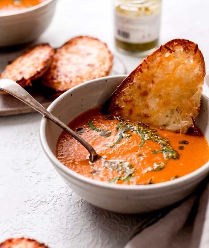 white ceramic bowl, filled with cream soup, cream of mushroom soup recipe, bread dipped in it, pesto sauce garnish