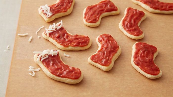 stockings shaped dough, covered with tomato sauce and cheese, arranged on wooden board, holiday appetizers