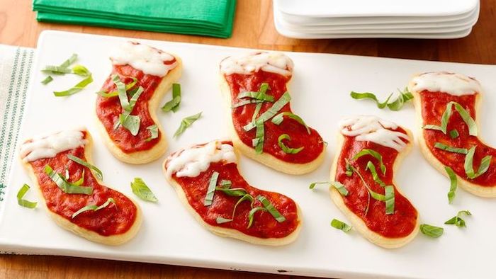 stockings shaped dough, tomato sauce cheese and chopped basil leaves on top, arranged on white board, holiday appetizers