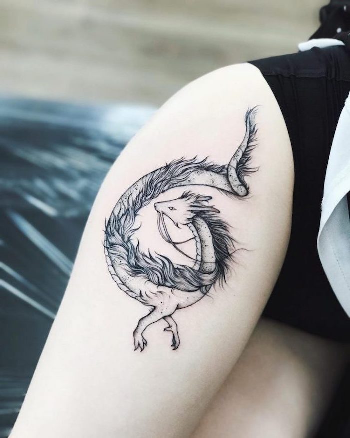 dragon forearm tattoo, thigh tattoo, on woman wearing black shorts, lying on black leather bed