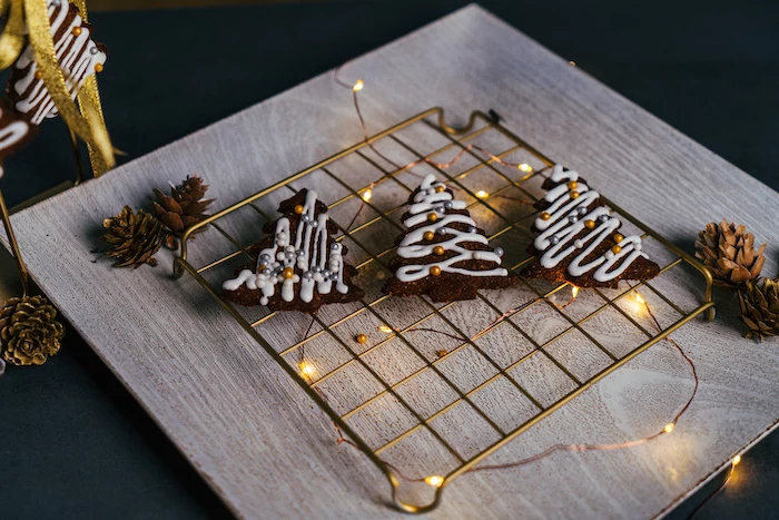 three christmas tree shaped cookies, decorated with royal icing and sugar pearls, vegan gingerbread cookies, placed on metal rail