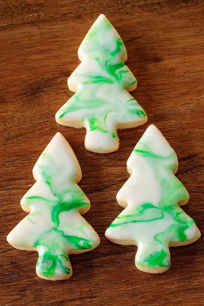 three christmas tree shaped cookies, placed on wooden surface, white and green icing on top, christmas cookie decorating ideas