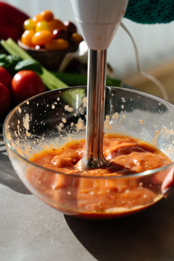 tomatoes in glass bowl, pureed with hand mixer, tomato soup, grey countertop, blurred background
