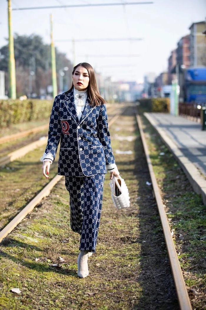 woman walking on train tracks, 2019 style trends, wearing blue suit with trousers and blazer, white heels and bag