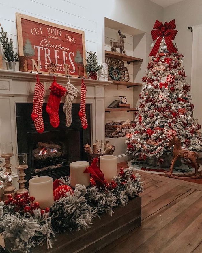 red and silver ornaments, on a tree with faux snow, tree decorating ideas, large red ribbon on top, placed next to the fireplace