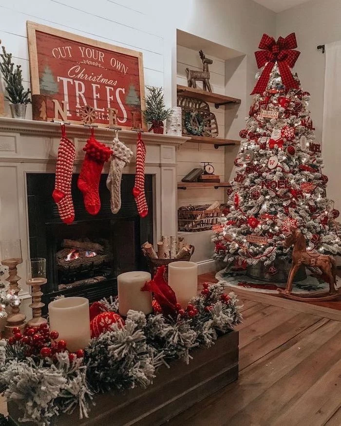 red and silver ornaments, on a tree with faux snow, tree decorating ideas, large red ribbon on top, placed next to the fireplace