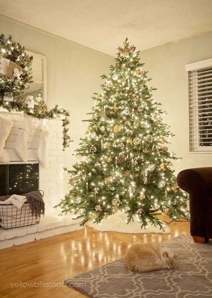tree decorated with lots of lights, gold ornaments and pine cones, white christmas tree decor, cat sleeping on the floor next to it