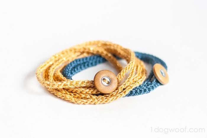 two crochet bracelets in blue and gold, with brown leather buttons, placed on white surface, gifts for boyfriend, step by step diy tutorial