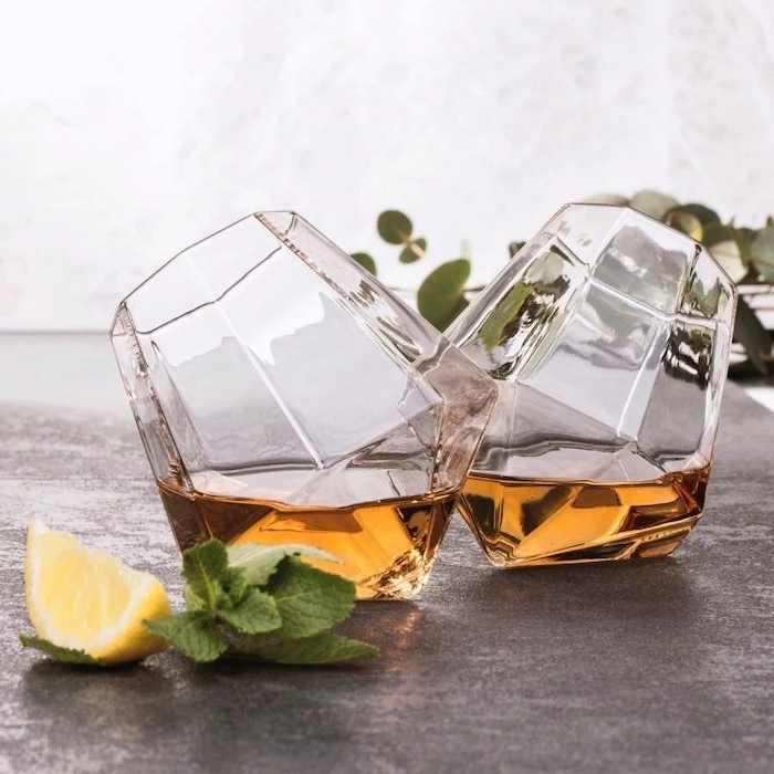 two diamond shaped crystal whiskey glasses, placed on grey surface, christmas gift ideas for him, mint leaves and lemon slices on the side