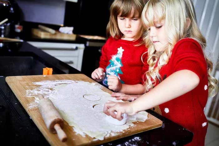 two little girls baking, how to make ornaments, dough rolled out on wooden board, placed on black surface