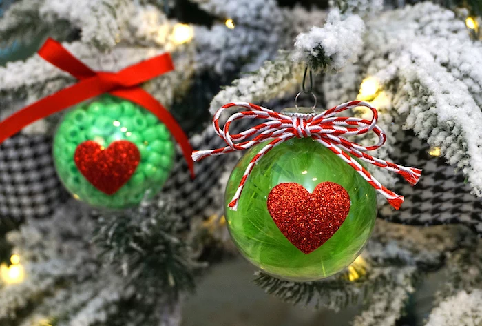 two plastic baubles, filled with green beads, with red glittery hearts, easy christmas crafts for kids, hanged with red bows