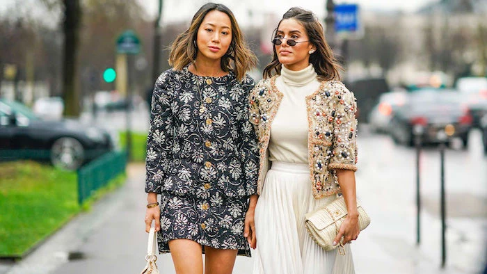 two women walking down the street, 2019 style trends, one wearing floral dress, another all white outfit with beige jacket