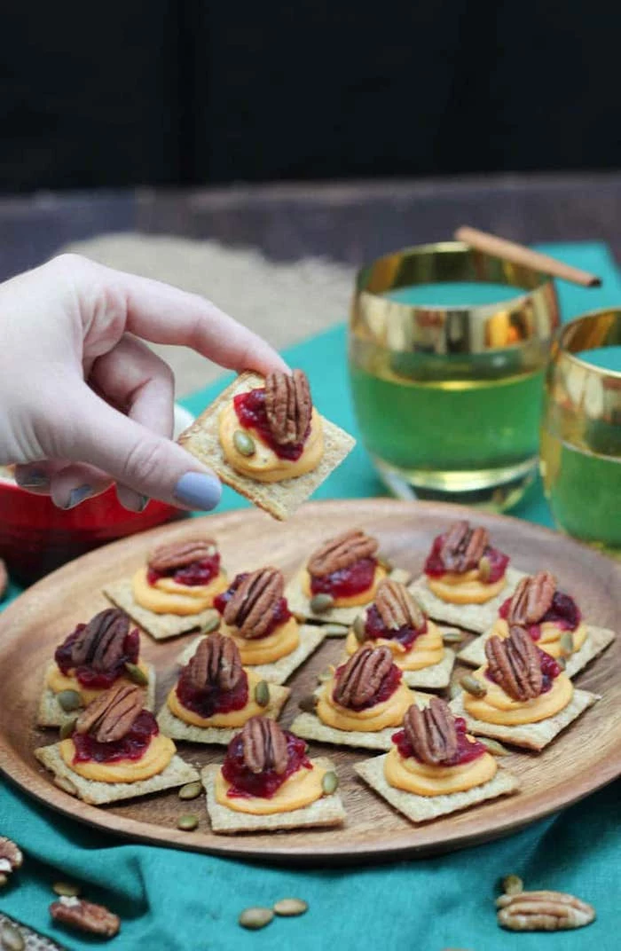 vegan bites, easy party snacks, crackers with sweet potato puree, cranberry sauce and walnuts, placed on wooden plate