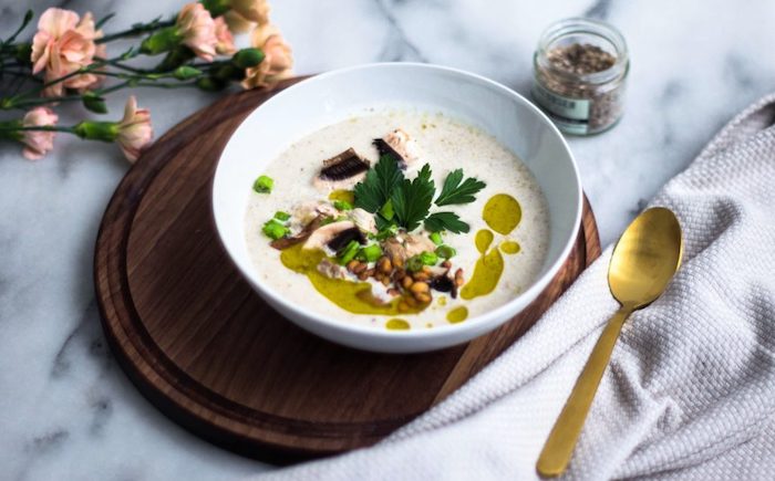 cream of chicken soup recipe, nuts and fresh herbs for garnish, white ceramic bowl, on wooden board, on marble countertop