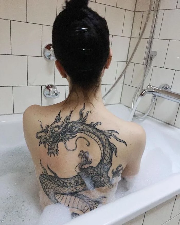 dragon thigh tattoo, large back tattoo, on woman sitting in bathtub, with black hair in a messy bun