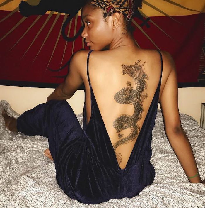 large back tattoo, dragon thigh tattoo, woman wearing blue velvet onesie, with open back, sitting on a bed