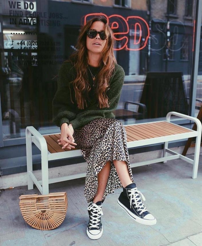 woman sitting on a wooden bench, clothing trends 2019, wearing silk leopard print skirt, green sweater and converse sneakers