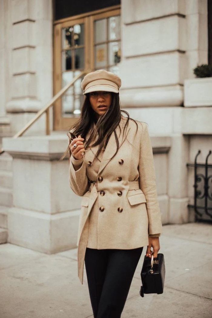 woman with long brown hair, new york winter fashion, wearing black trousers, beige coat and hat, small clutch bag