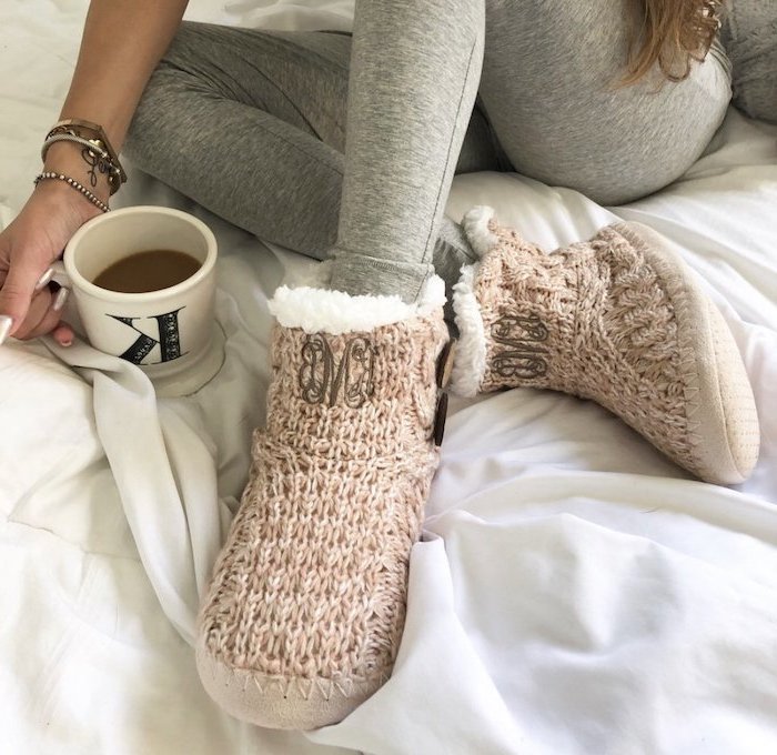 what to get mom for christmas, woman sitting in bed, wearing grey tights and knitted slippers, holding a coffee mug