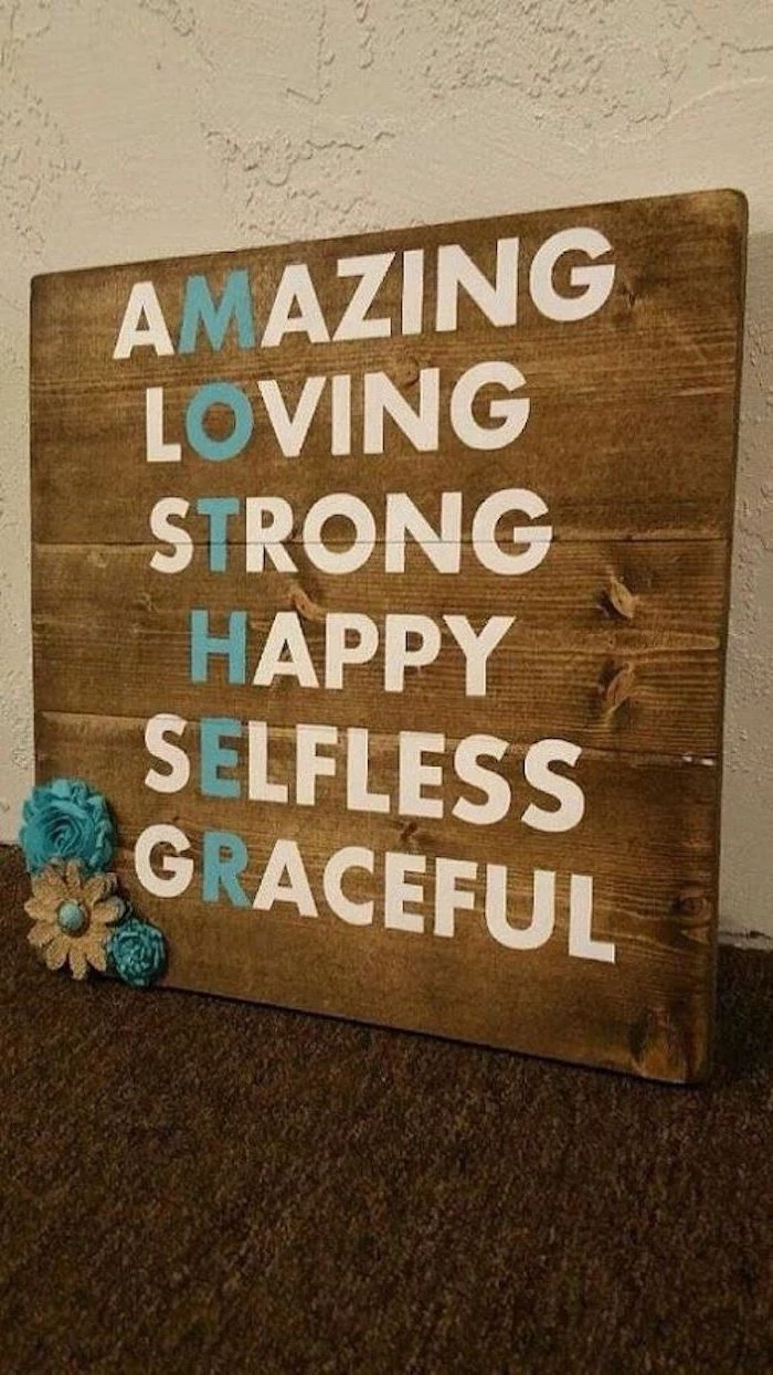 wooden board with adjectives written on it, forming the word mother, meaningful gifts for mom, leaning on white wall