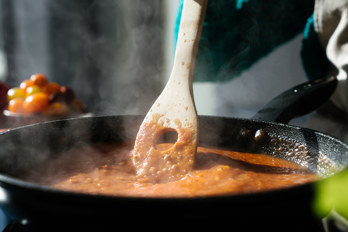 tomato puree in black sauce pan, stirred with wooden spatula, tomato soup recipe, blurred background