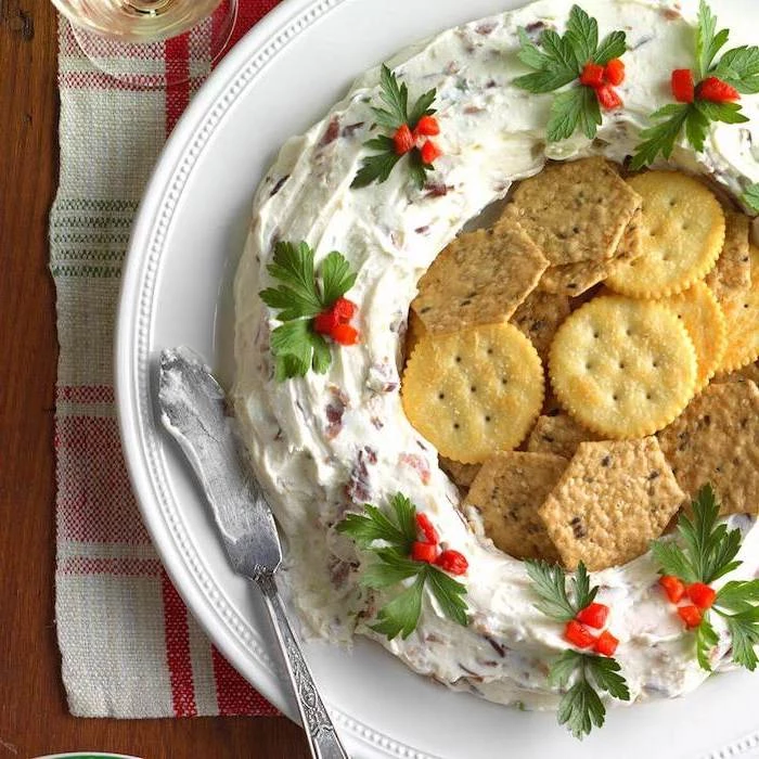 wreath made of bacon and cheese dip, crackers in the middle, christmas party snacks, placed on white plate