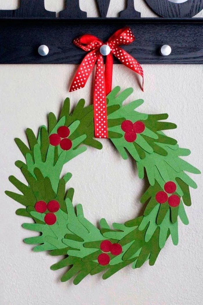 christmas wreath made of handprints, cut out of green paper, hung with red ribbon, homemade christmas crafts