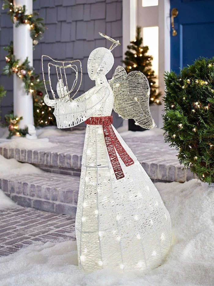 angel figurine, intertwined with lights, large outdoor christmas decorations, red ribbon tied around it, placed in the snow