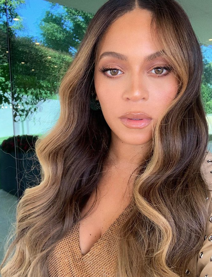 beyonce with brown hair with blonde highlights, curly hair color ideas, wearing nude top, long wavy hair