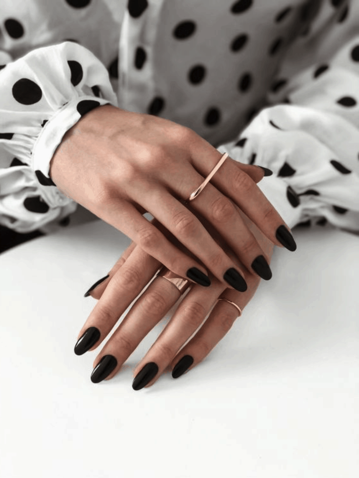 woman with almond nails, wearing white shirt with black polka dots, winter nail colors, black nail polish