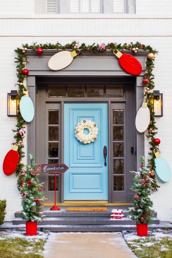 wreath with red baubles, hanging over the door frame, outdoor christmas tree lights, blue door with white wreath