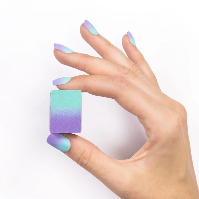 female hand holding a sponge, with short squoval nails, ombre nails, turquoise and purple gradient nail polish