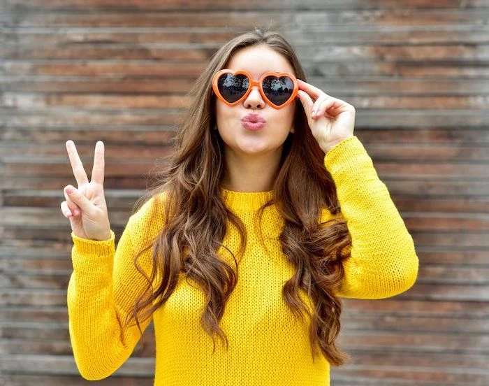 woman wearing yellow knitted sweater, heart shaped orange sunglasses, hair color trends 2020, long brown wavy hair