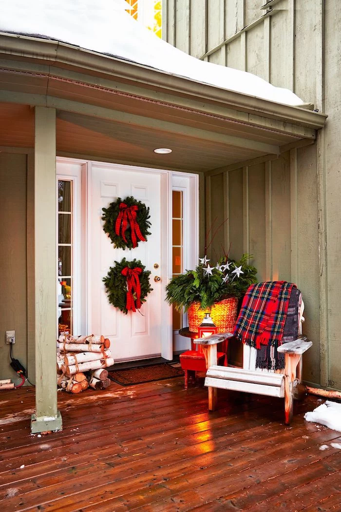 wooden chair with plaid blanket on the porch, outdoor christmas decorations, two christmas wreaths with red ribbons on the door