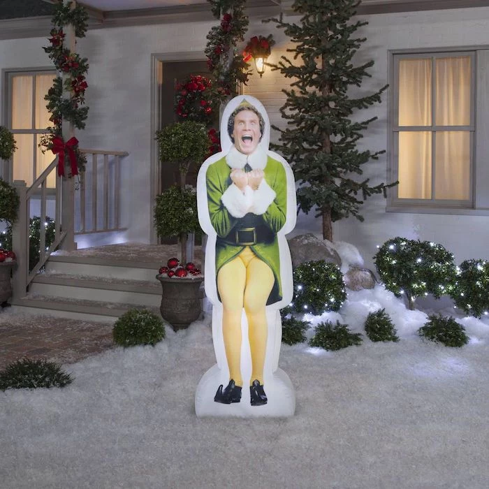will ferrell character from movie elf, outdoor christmas tree lights, figurine placed in the snow, in the front yard