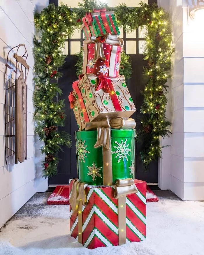 faux presents with lights, placed in the snow in front of a door, christmas porch decorations, wreath with lights on the door frame