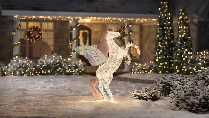 unicorn figurine, intertwined with lights, placed in the snow, in front of a house decorated with lights, christmas porch decorations