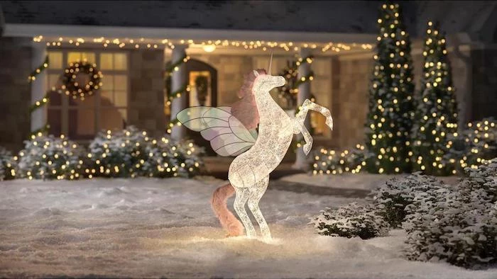 unicorn figurine, intertwined with lights, placed in the snow, in front of a house decorated with lights, christmas porch decorations