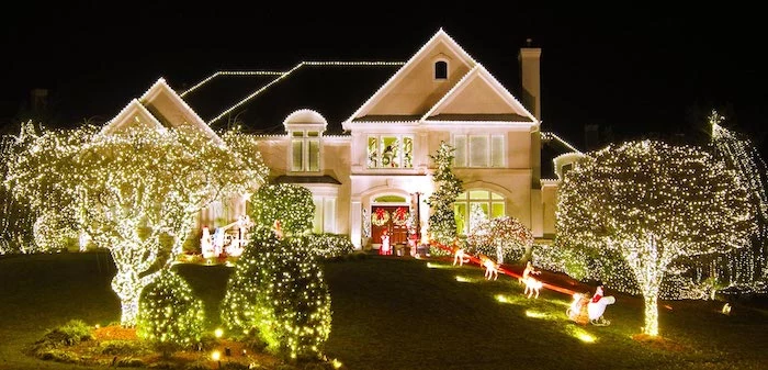 two storey house, decorated with lights, christmas porch decorations, lots of trees and bushes, decorated with lights