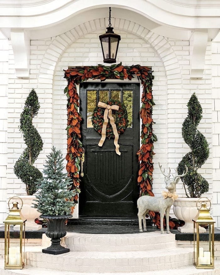 wreath with fall leaves, hanging over door frame, front porch christmas decorations, trees and lanterns on both sides