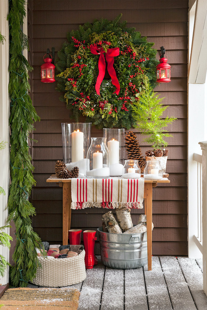 green wreath with berries, hanging over wooden table, candles and pine cones on it, outdoor lighted christmas decorations